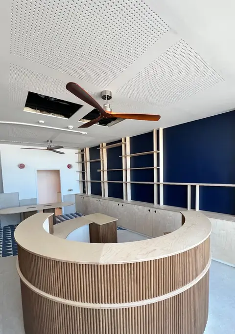 Bar courbe habillé de lames de bois, sous un plafond perforé avec ventilateur.