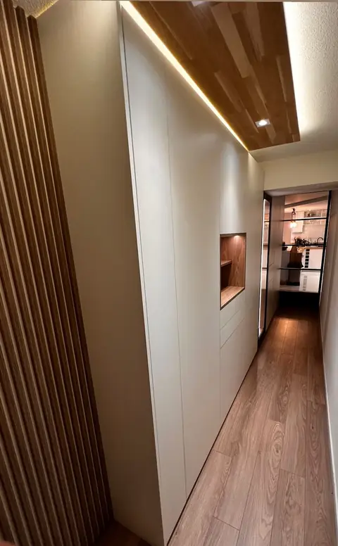 Couloir bordé de placards blancs intégrés et de lames de bois, plafond en bois éclairé.