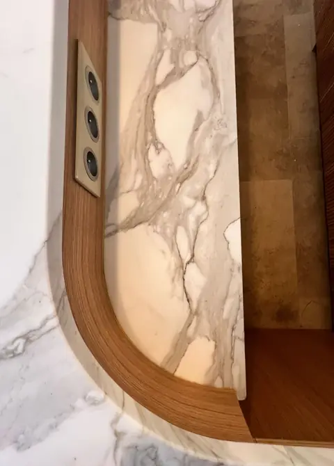 Détail d'un habillage courbe en bois bordant un panneau de marbre blanc veiné.