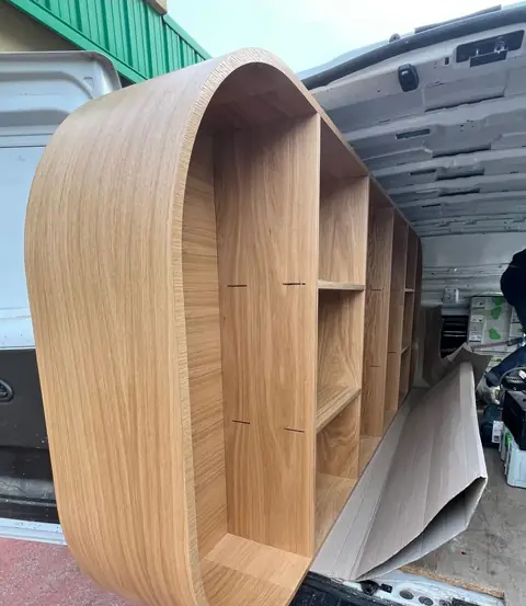 Meuble ovale en bois clair aux bords arrondis, chargé dans un camion avant la pose.