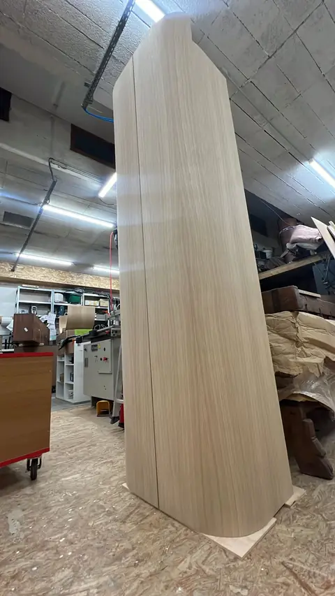 Haut élément en bois aux bords cintrés, debout dans l'atelier.