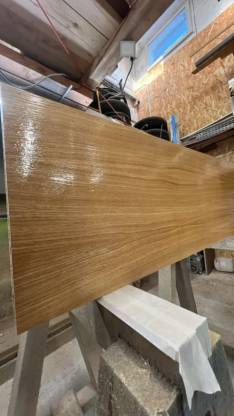 Panneau plaqué bois fraîchement verni, brillant sous la lumière de l'atelier.