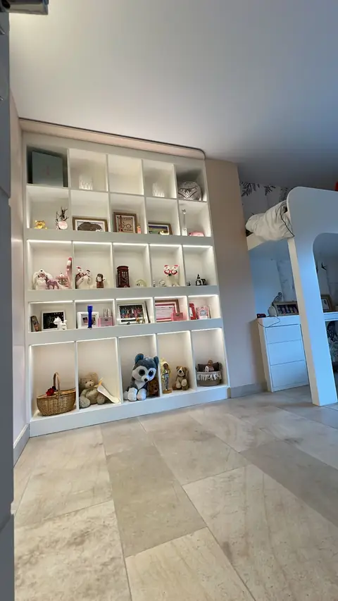 Bibliothèque blanche à cases éclairées garnie de livres et de jouets.