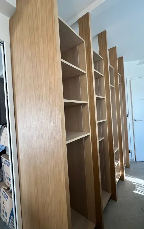 Bibliothèque haute en bois clair aux étagères régulières.