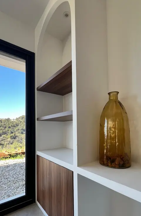 Niches blanches avec étagères et façade en bois foncé, près d'une baie vitrée.