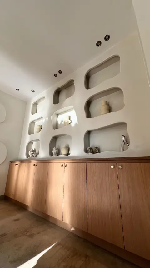 Mur blanc creusé de niches aux angles arrondis, au-dessus de meubles bas en bois.
