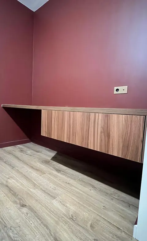 Long bureau suspendu en bois devant un mur rouge foncé.
