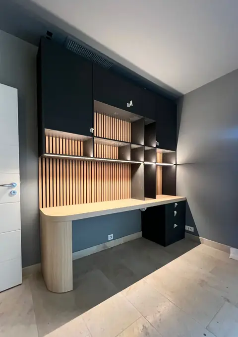 Bureau aux angles arrondis en bois clair, habillage à tasseaux et rangements noirs.