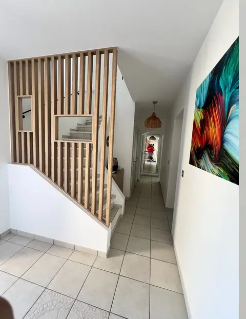 Claustra en lames de bois clair longeant un escalier dans un couloir.