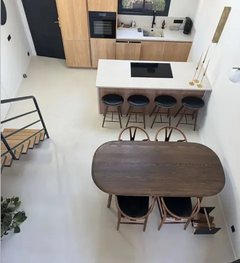 Vue plongeante sur une cuisine en bois avec îlot blanc, tabourets et table ovale en bois.