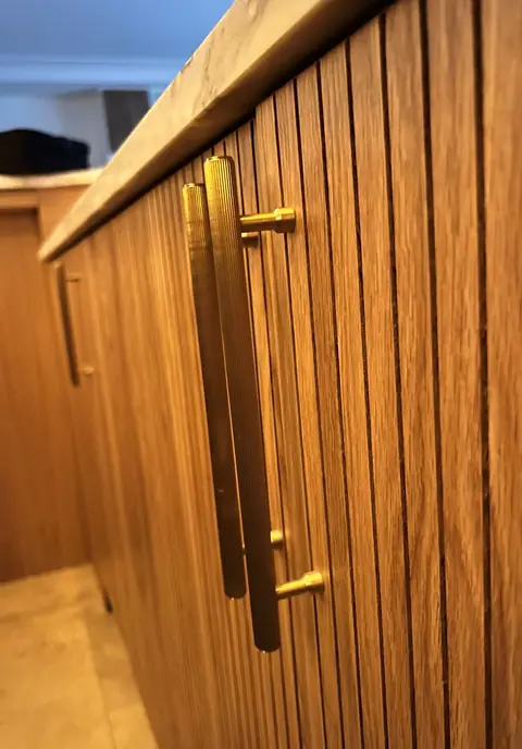Façade de cuisine en bois cannelé avec une longue poignée dorée.