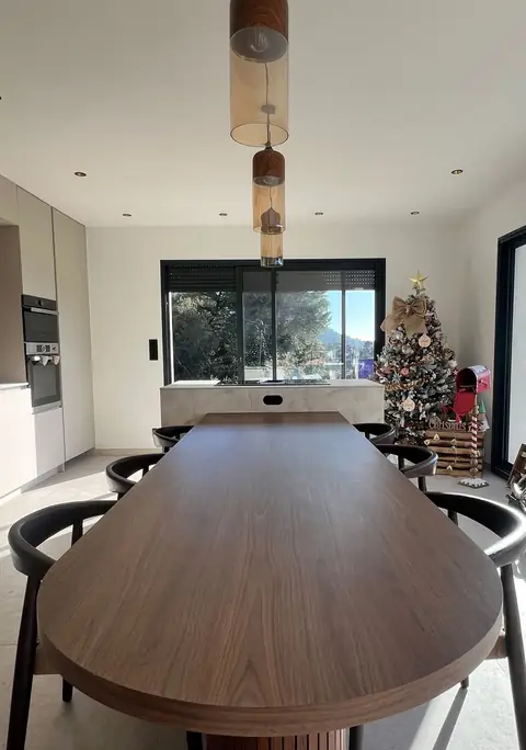 Long îlot-table en bois foncé aux bords arrondis, entouré de chaises, dans une cuisine ouverte.
