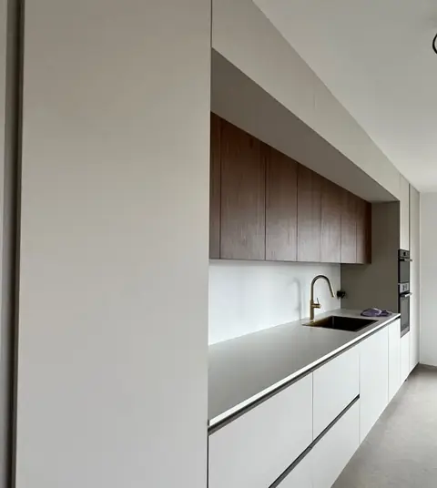 Cuisine linéaire aux façades blanches sans poignée, avec meubles hauts en bois foncé.