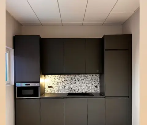Cuisine linéaire aux façades noires mates, avec four en colonne et crédence en terrazzo.