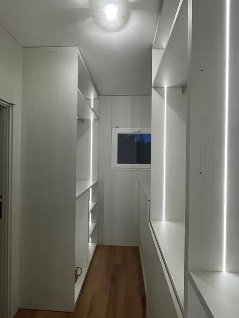 Dressing en couloir blanc, avec rangements des deux côtés et éclairage LED dans les montants.