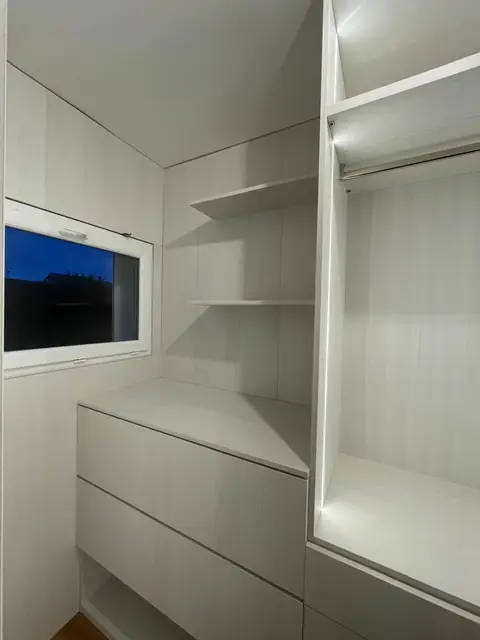 Dressing blanc avec étagères, tiroirs sous la fenêtre et penderie éclairée par LED.
