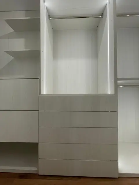 Dressing blanc avec penderie éclairée par LED, étagères et colonne de tiroirs.