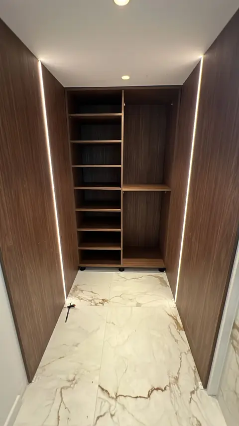 Dressing en bois foncé avec étagères et éclairage LED intégré dans les montants.