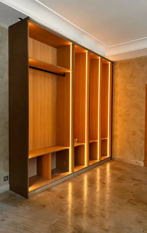 Dressing ouvert en bois clair, avec penderies, niches et éclairage intégré.