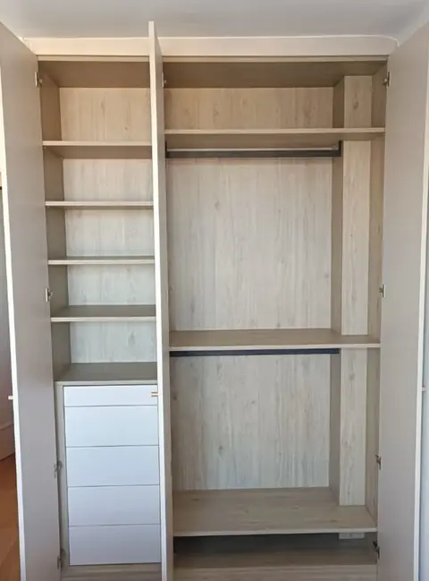 Dressing en bois clair avec étagères, penderie et colonne de tiroirs blancs.