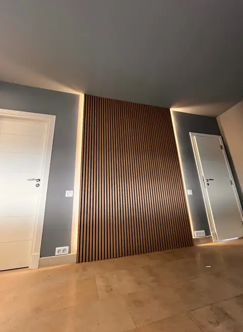 Mur habillé de tasseaux en bois foncé, encadré d'un éclairage LED.