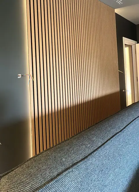Tête de lit murale en tasseaux de bois avec éclairage latéral.
