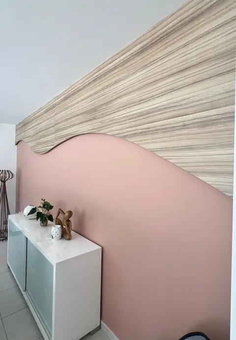Panneau mural en bois veiné découpé en forme de vague sur un mur rose.