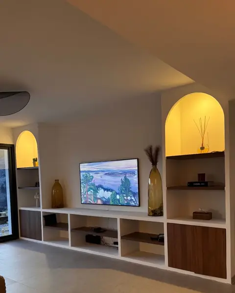 Meuble TV bas blanc et bois, encadré de niches en arche éclairées.