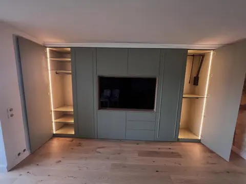 Mur de rangements sur mesure intégrant un écran TV, avec niches éclairées de chaque côté.
