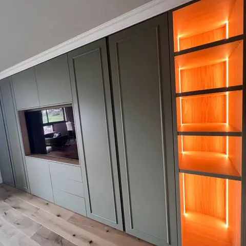 Mur de rangements vert intégrant un écran, avec niches rétroéclairées orange.