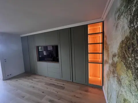 Mur de rangements vert terminé par une vitrine aux étagères éclairées en orange.