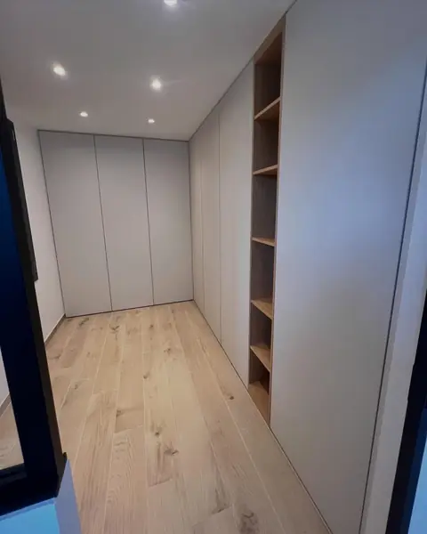 Placards blancs toute hauteur et étagères ouvertes en bois dans un couloir.