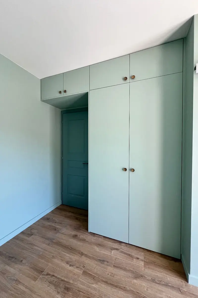 Placards sur mesure vert pâle installés sous un plafond en pente, autour d'une porte.