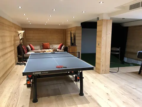 Salle de jeux au parquet de chêne et aux murs habillés de lames de bois, avec table de ping-pong et canapé.