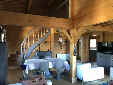 Séjour de chalet avec escalier tournant, poutres et murs en bois.