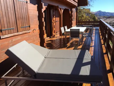 Terrasse en bois le long du chalet, avec bains de soleil et table.