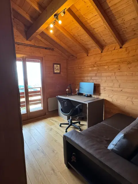 Bureau installé sous la charpente, devant une porte-fenêtre.
